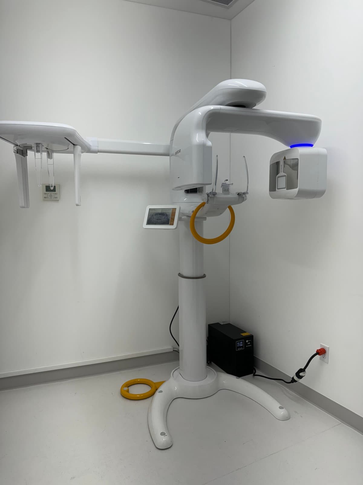 A panoramic dental X-ray unit stands in an empty white imaging room