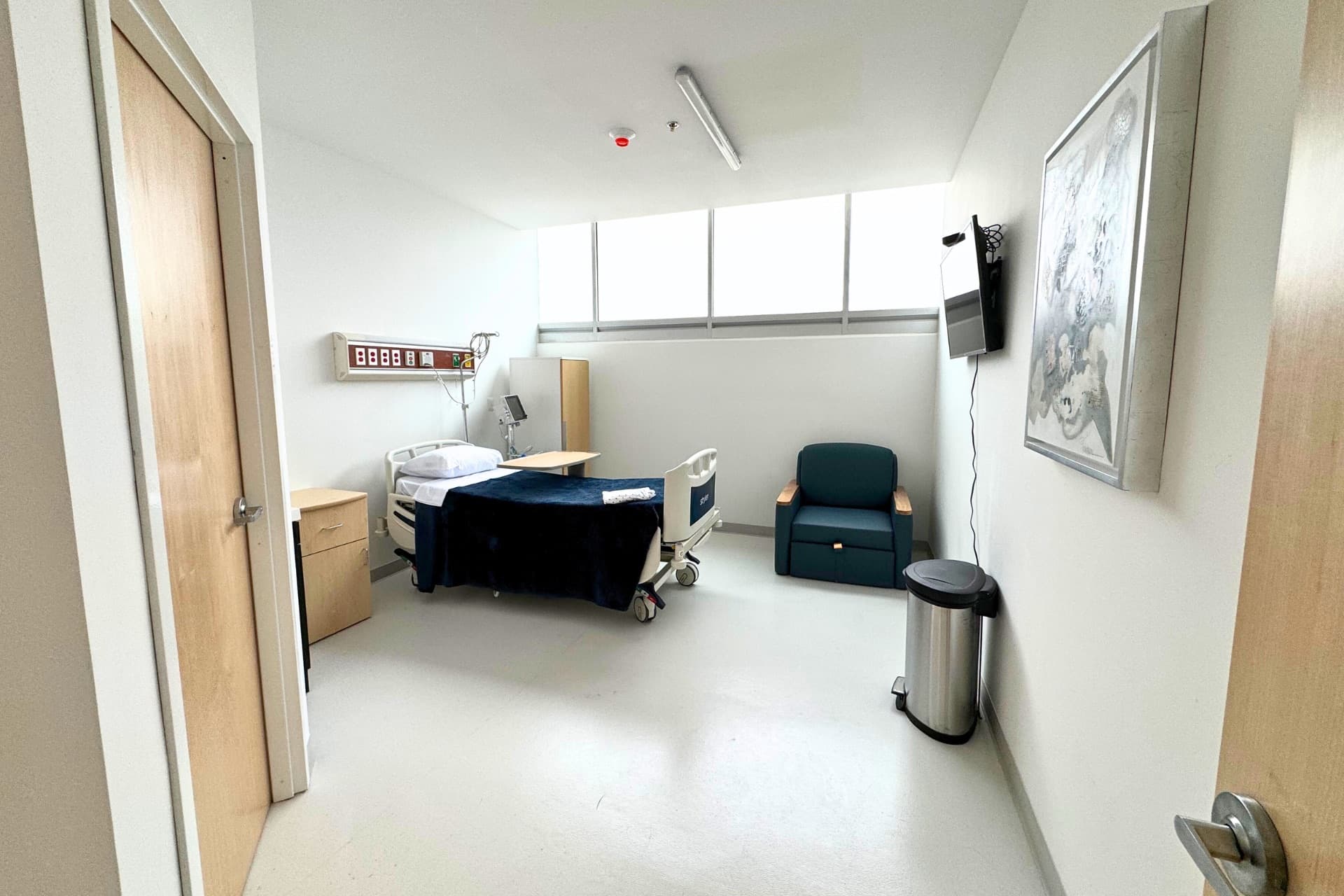 Private hospital room with a patient bed, a recliner chair, a window and framed artwork on the wall