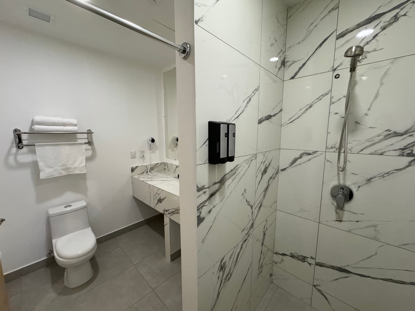 Private bathroom with a marble-tiled walk-in shower, toilet, basin and folded towels on a rail