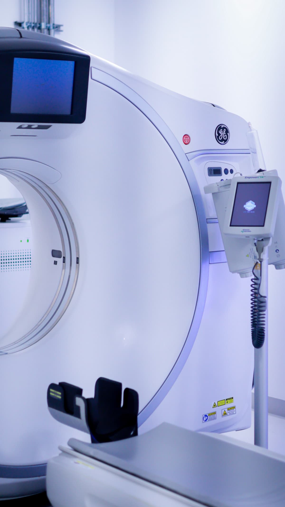 Side of a CT gantry showing the control display and handheld remote on its cord