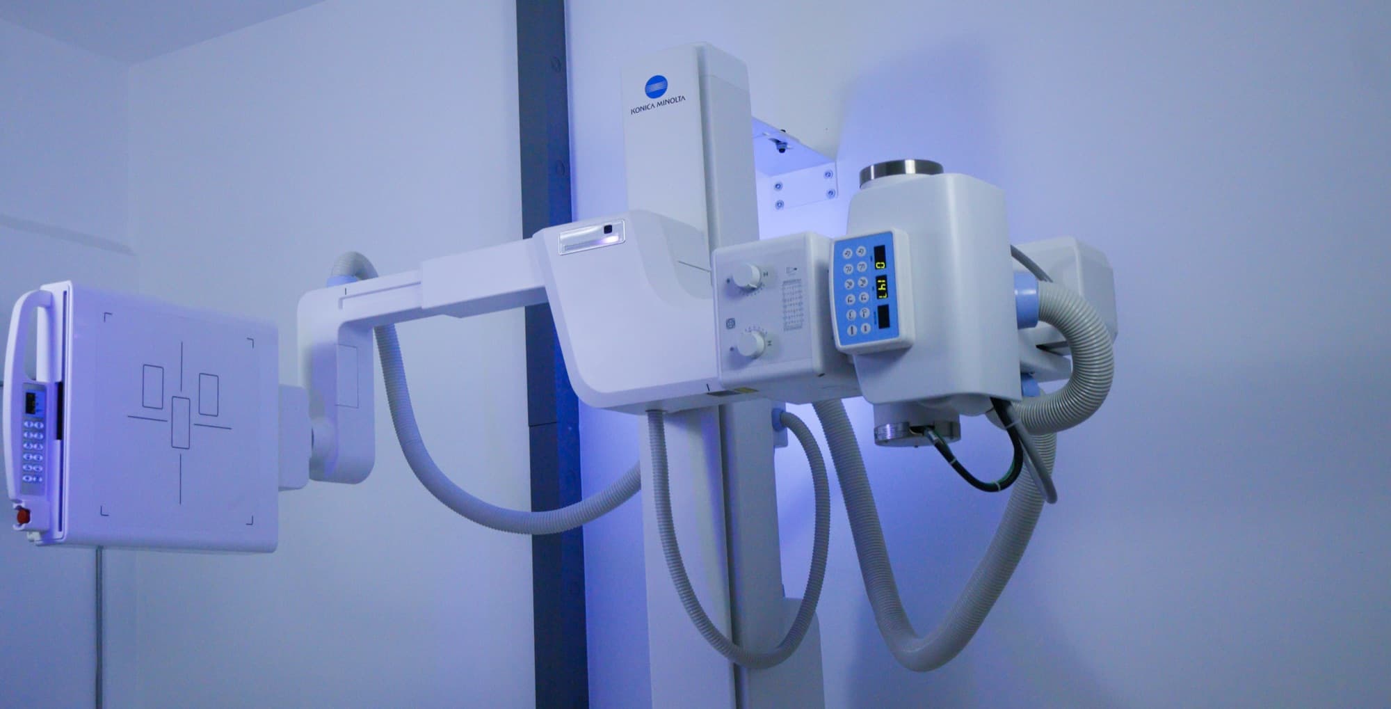X-ray tube head on a suspended arm facing a wall-mounted detector panel