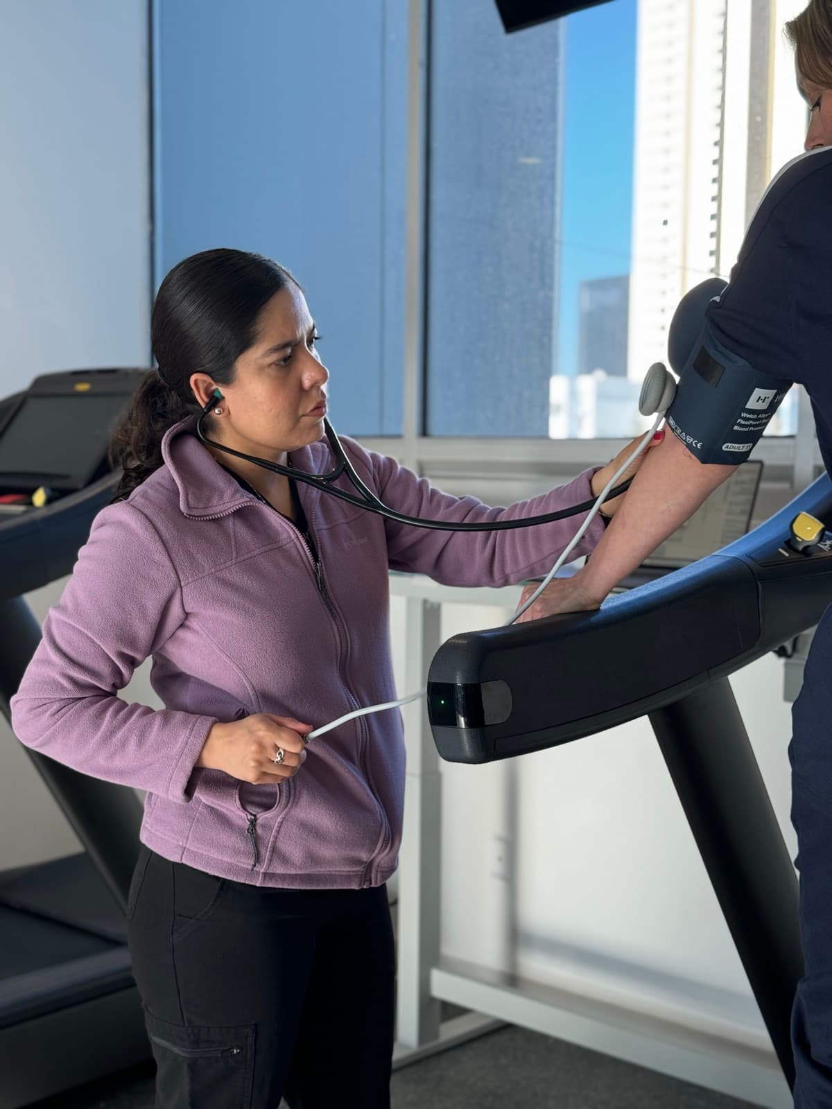 A clinician uses a stethoscope and an arm cuff to check a patient's blood pressure on a treadmill