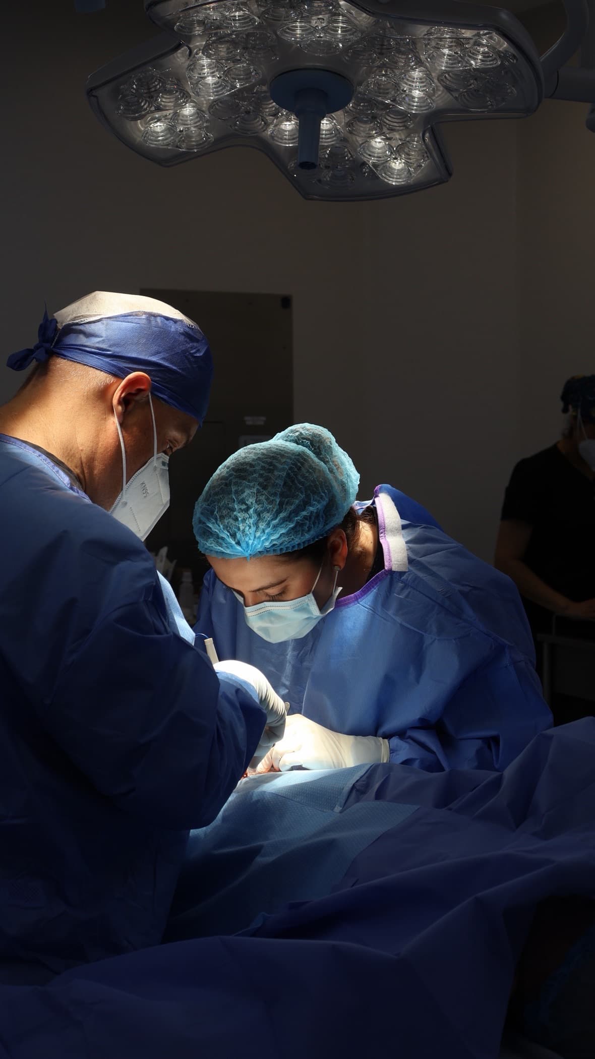 Two surgeons in scrubs, caps and masks operating at a draped surgical table